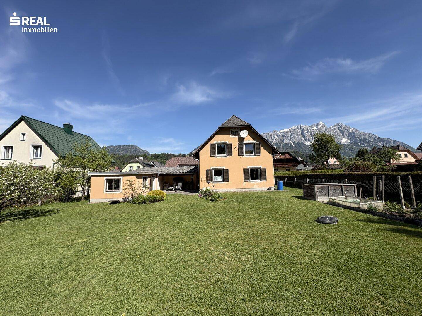 Weitläufiger Gartenbereich mit Haus und beeindruckendem Bergpanorama im Hintergrund.