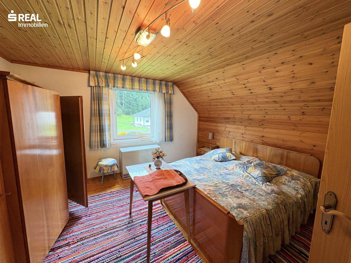 Gemütliches Schlafzimmer mit Holzvertäfelung, Teppichboden und Blick auf die Landschaft.