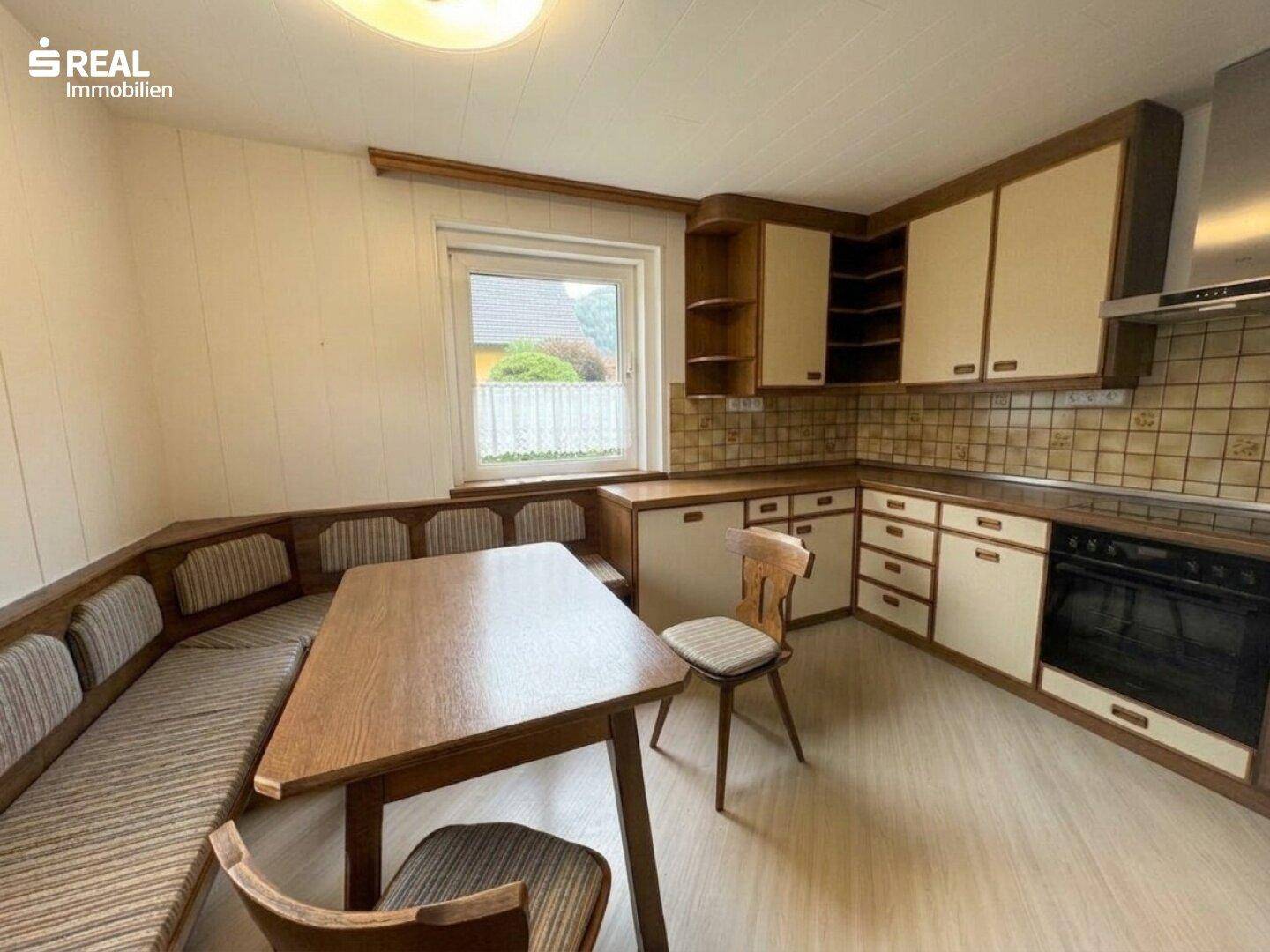 Traditionelle Wohnküche mit Eckbank, Holztisch und Einbauküche mit Fliesenrückwand.