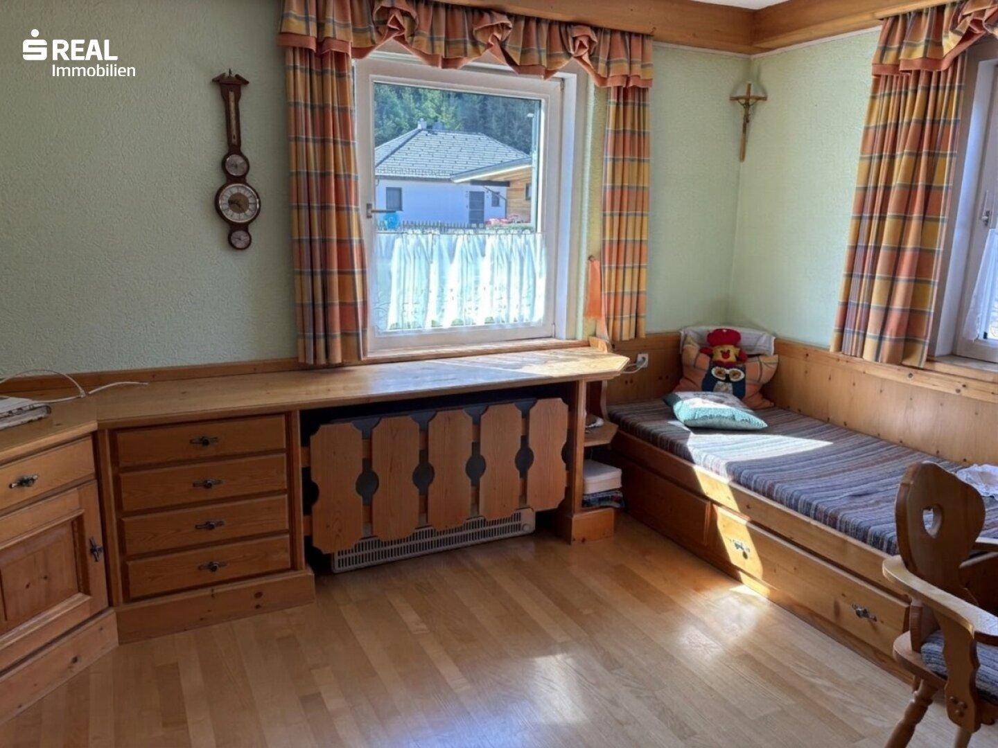 Traditionell eingerichteter Raum mit Holzmöbeln, integrierter Sitzbank und Blick ins Grüne.