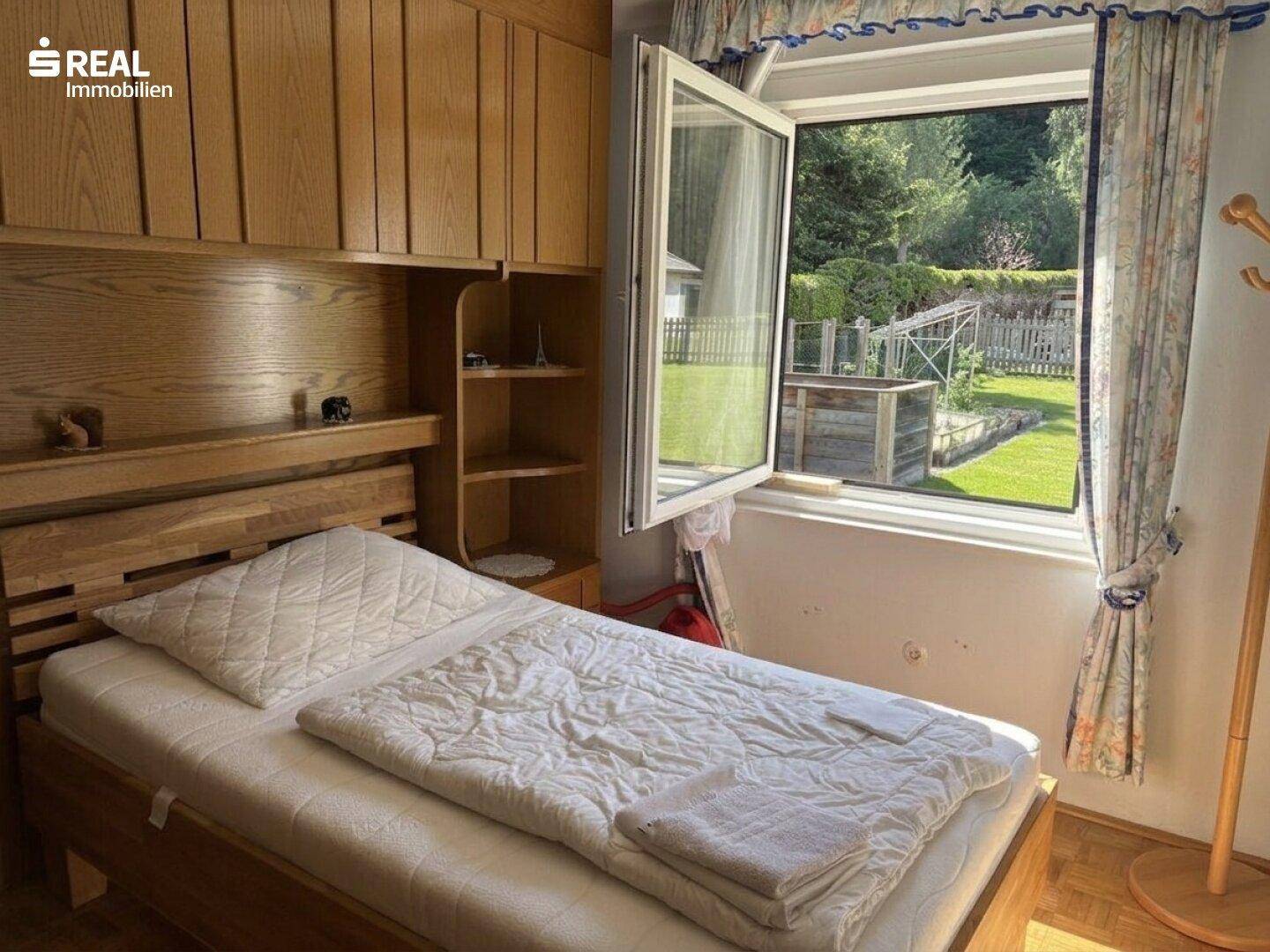 Helles Schlafzimmer mit Einzelbett, Einbauschränken und Fenster zum Gartenbereich.