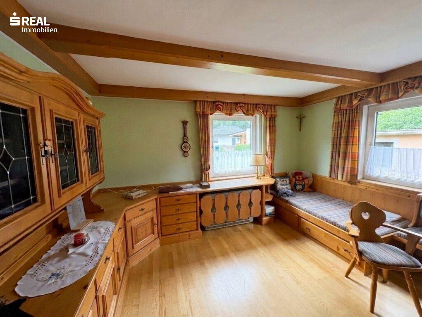 Gemütliches Wohnzimmer im alpinen Stil mit Holzbalken, Holzmöbeln und grünen Wänden.