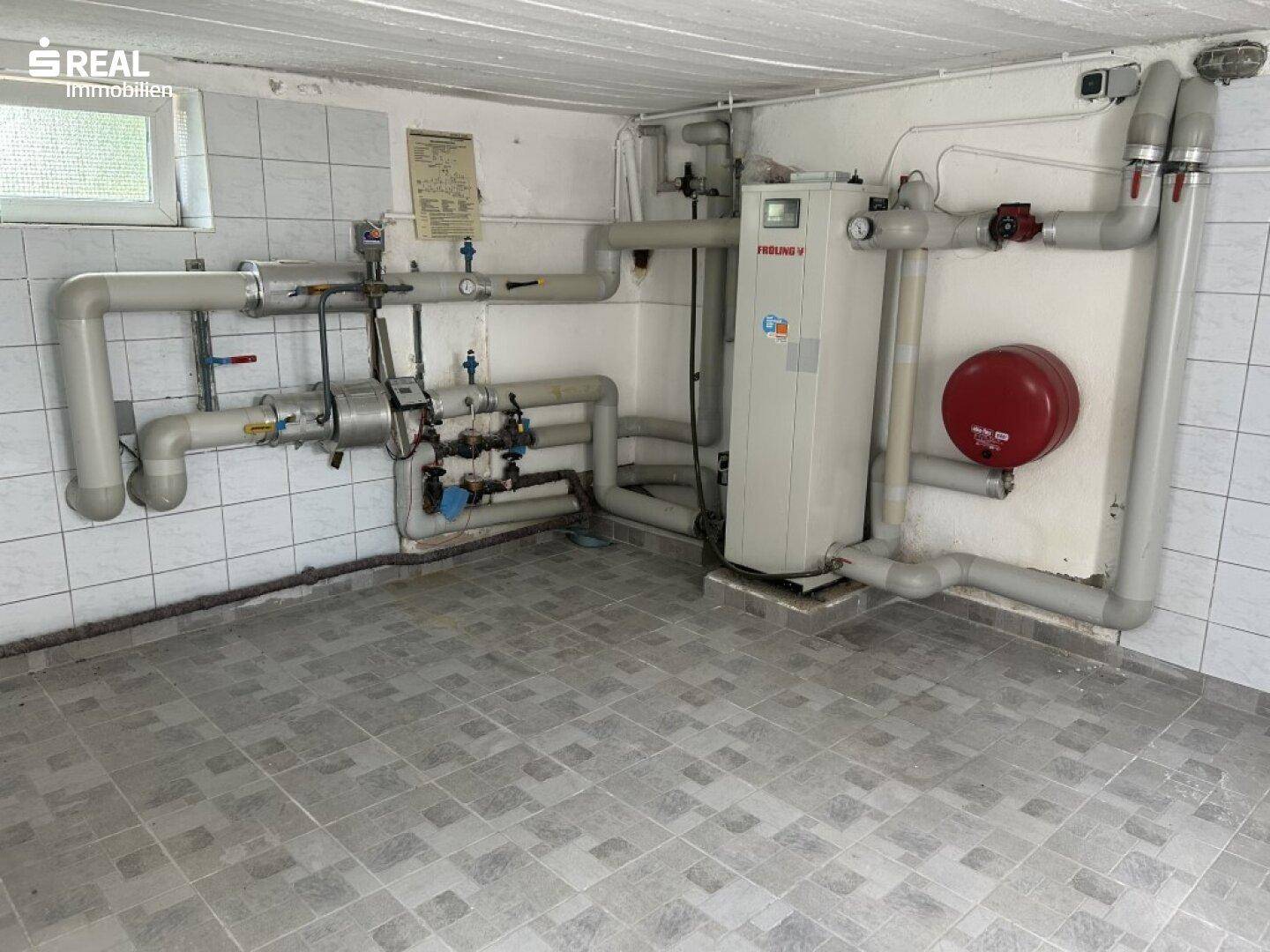 Technikraum im Keller mit Heizungsanlage, Rohrleitungen und gefliestem Boden.