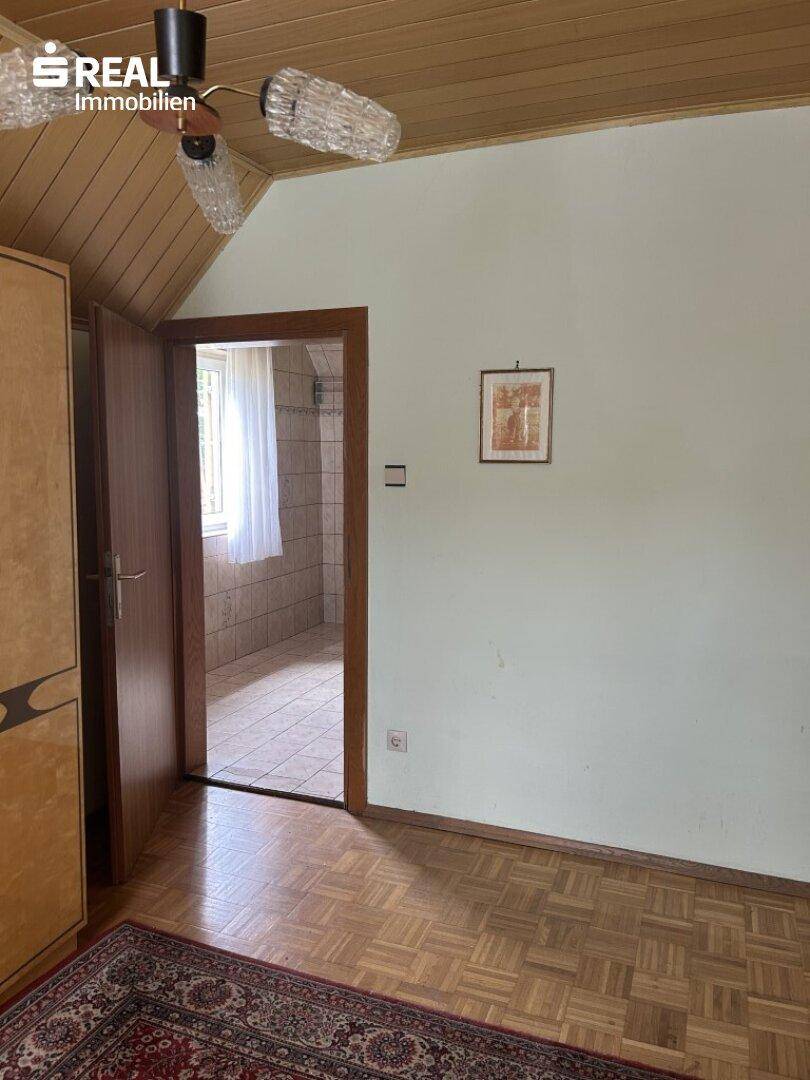Schlafzimmer mit Parkettboden, Holzdecke und Zugang zu einem gefliesten Badezimmer.