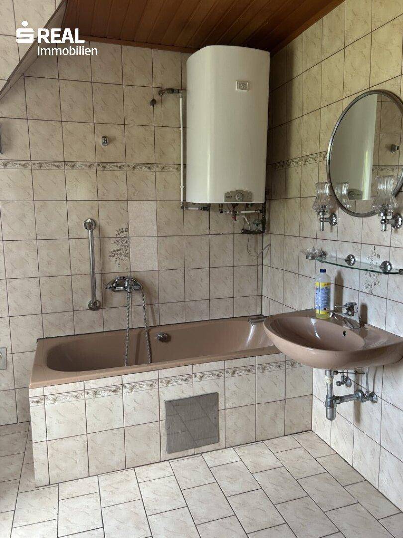 Badezimmer mit Badewanne, Waschbecken, Spiegel und Fliesen an Wänden und Boden.