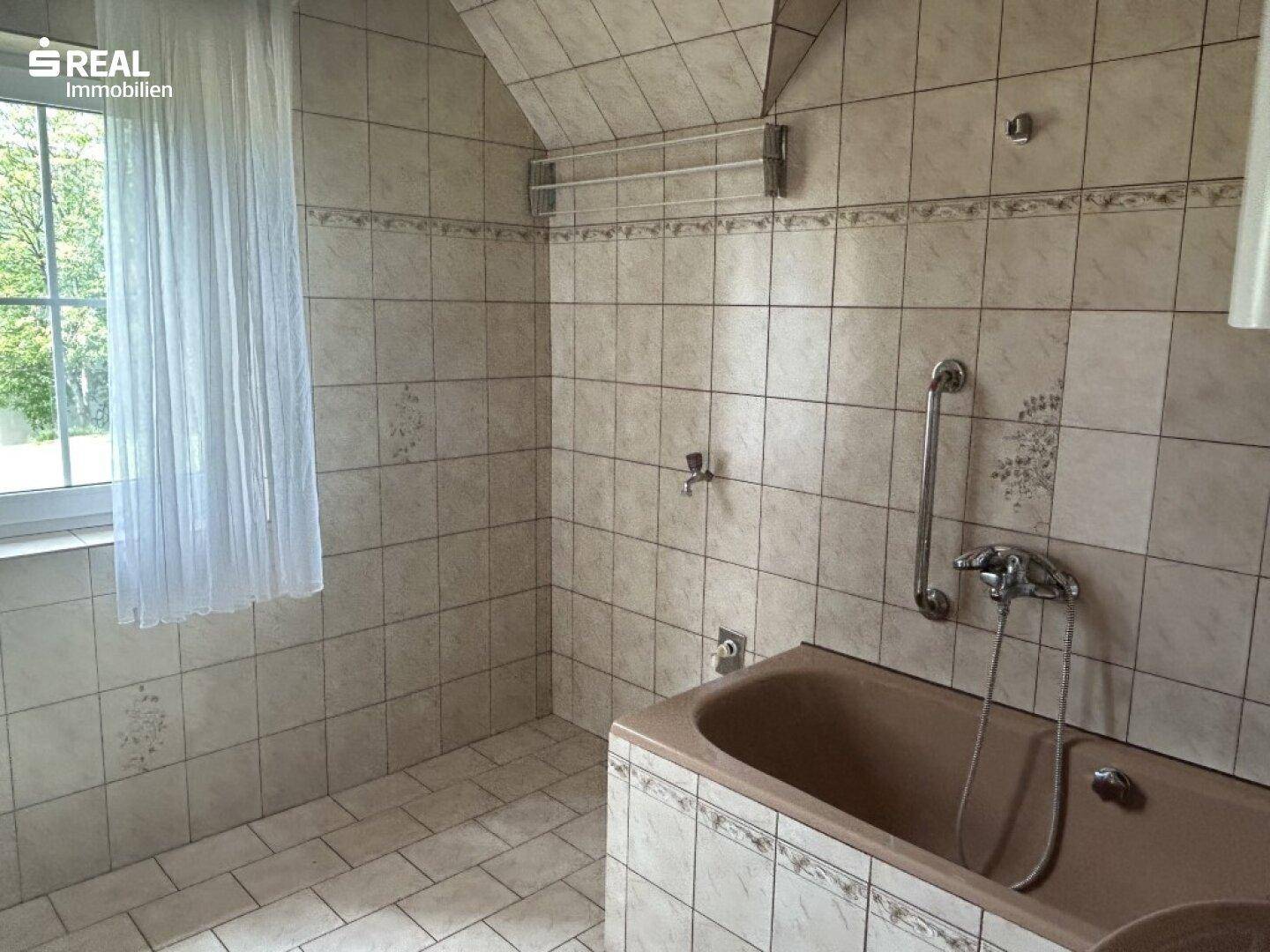 Helles Badezimmer mit Badewanne, Fliesen und einem Fenster für gute Belüftung.