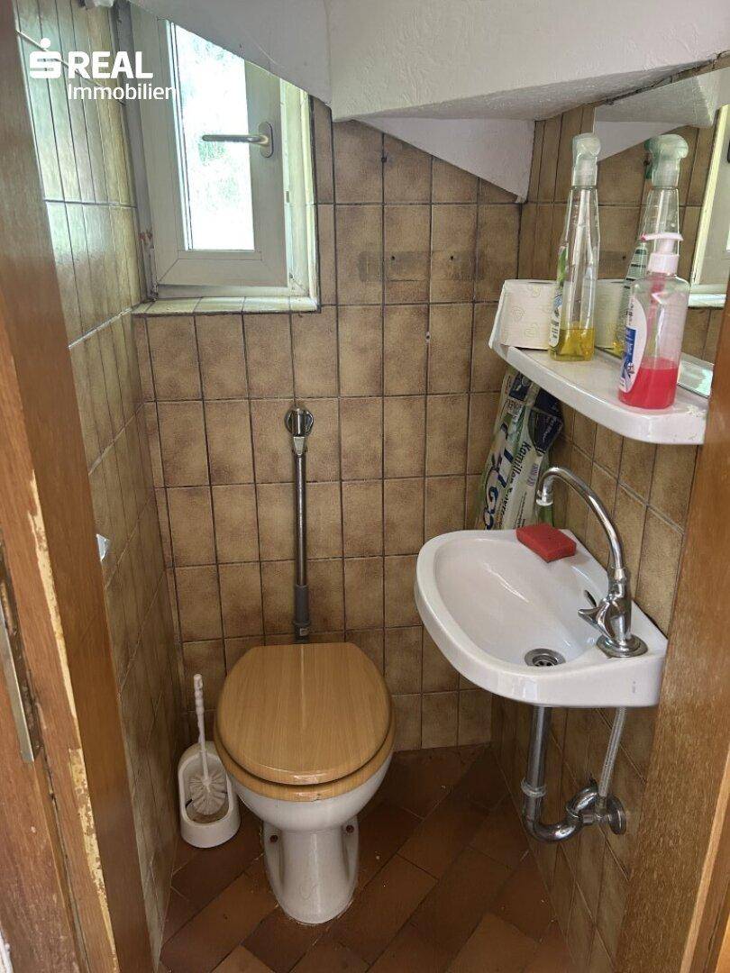 Kleines Gäste-WC mit Fliesenboden, Wandfliesen und einem Fenster für natürliche Belüftung.