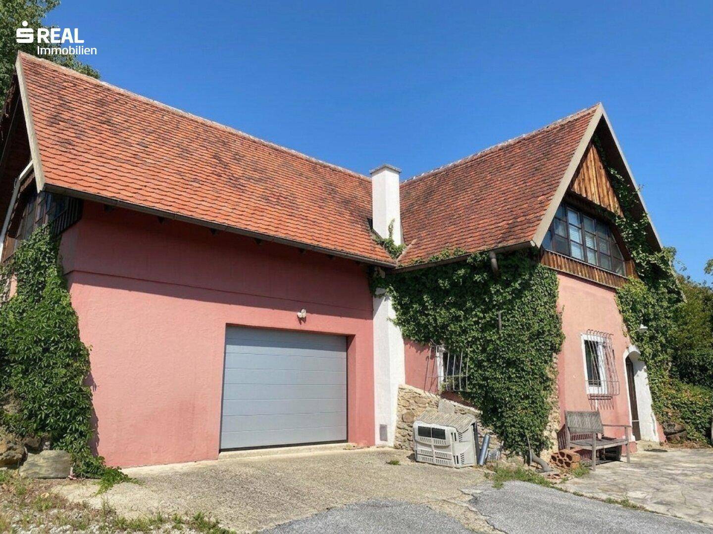 Ländliches Haus mit rotem Ziegeldach, Garage und Efeu an der Fassade.