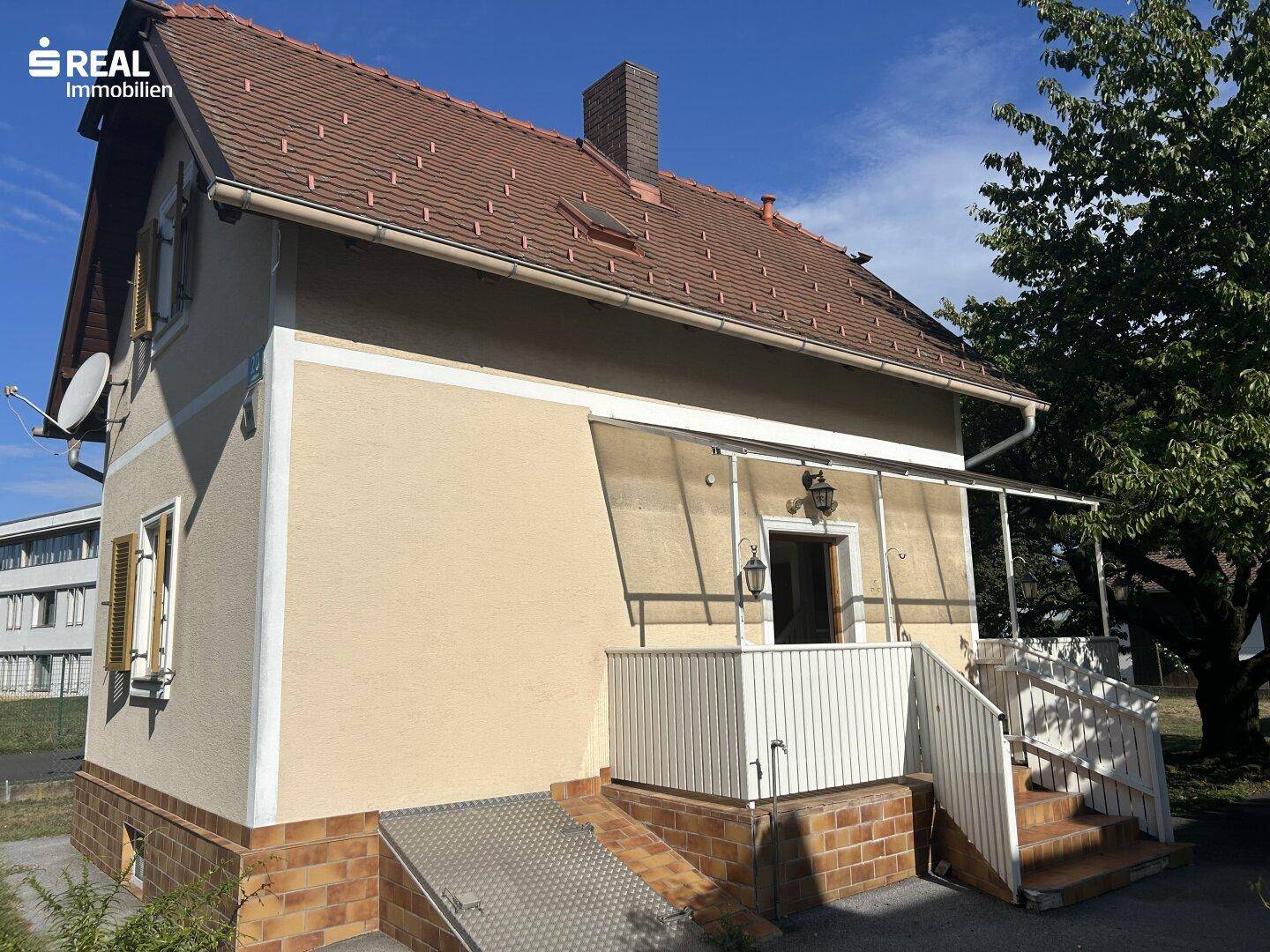 Seitenansicht des Hauses mit überdachtem Eingangsbereich, Treppe und kleiner Rampe.