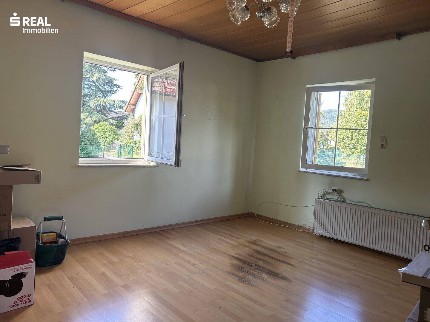Geräumiges Zimmer mit Parkettboden, Holzdecke und zwei großen Fenstern für viel Tageslicht.