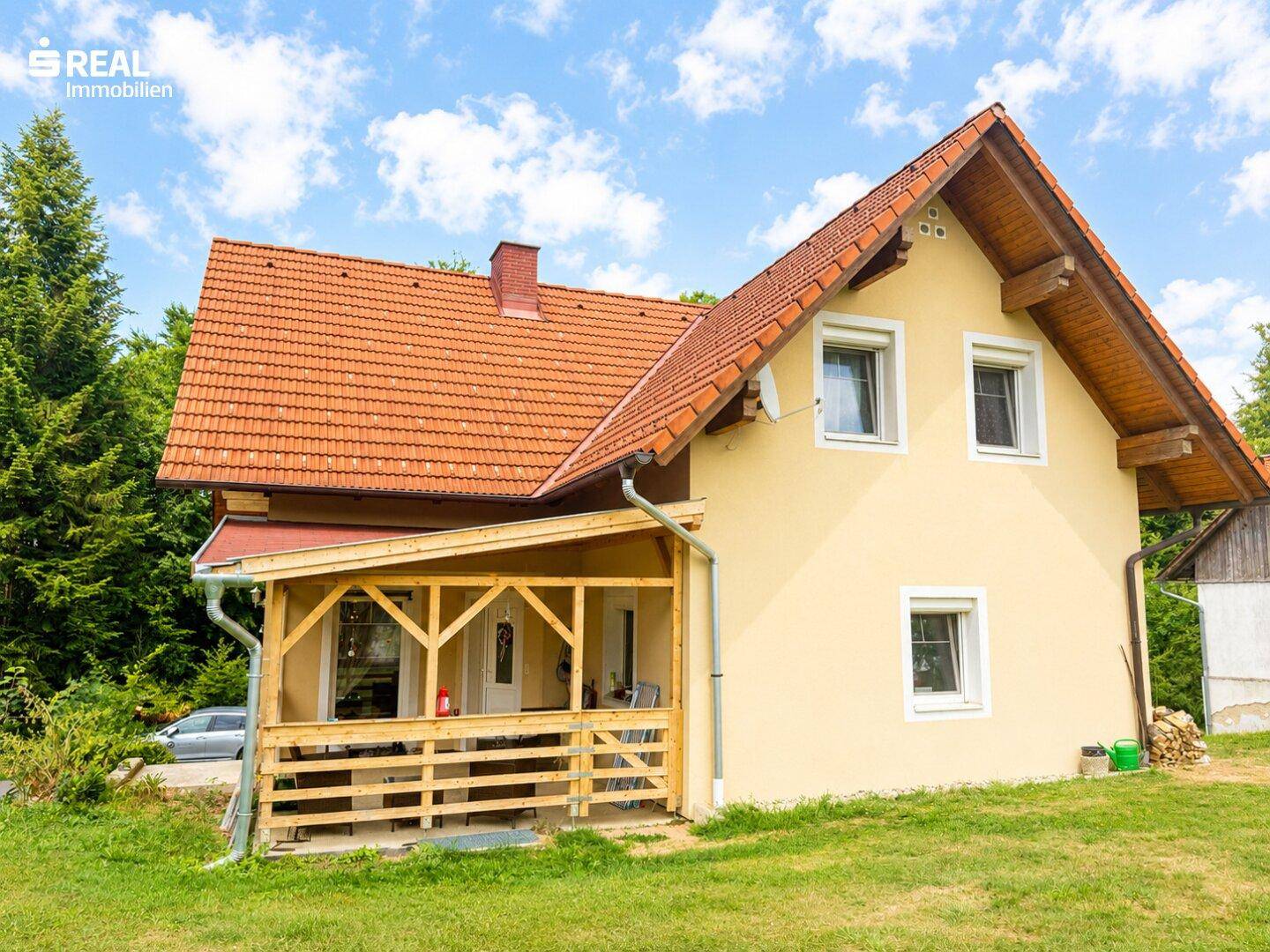 Rückansicht des Hauses mit überdachter Holzloggia und Blick ins Grüne.