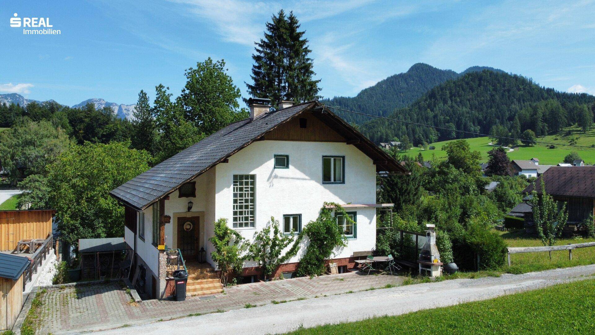 Vorderansicht des Hauses mit Eingangsbereich und gepflasterter Auffahrt, umgeben von Bäumen.