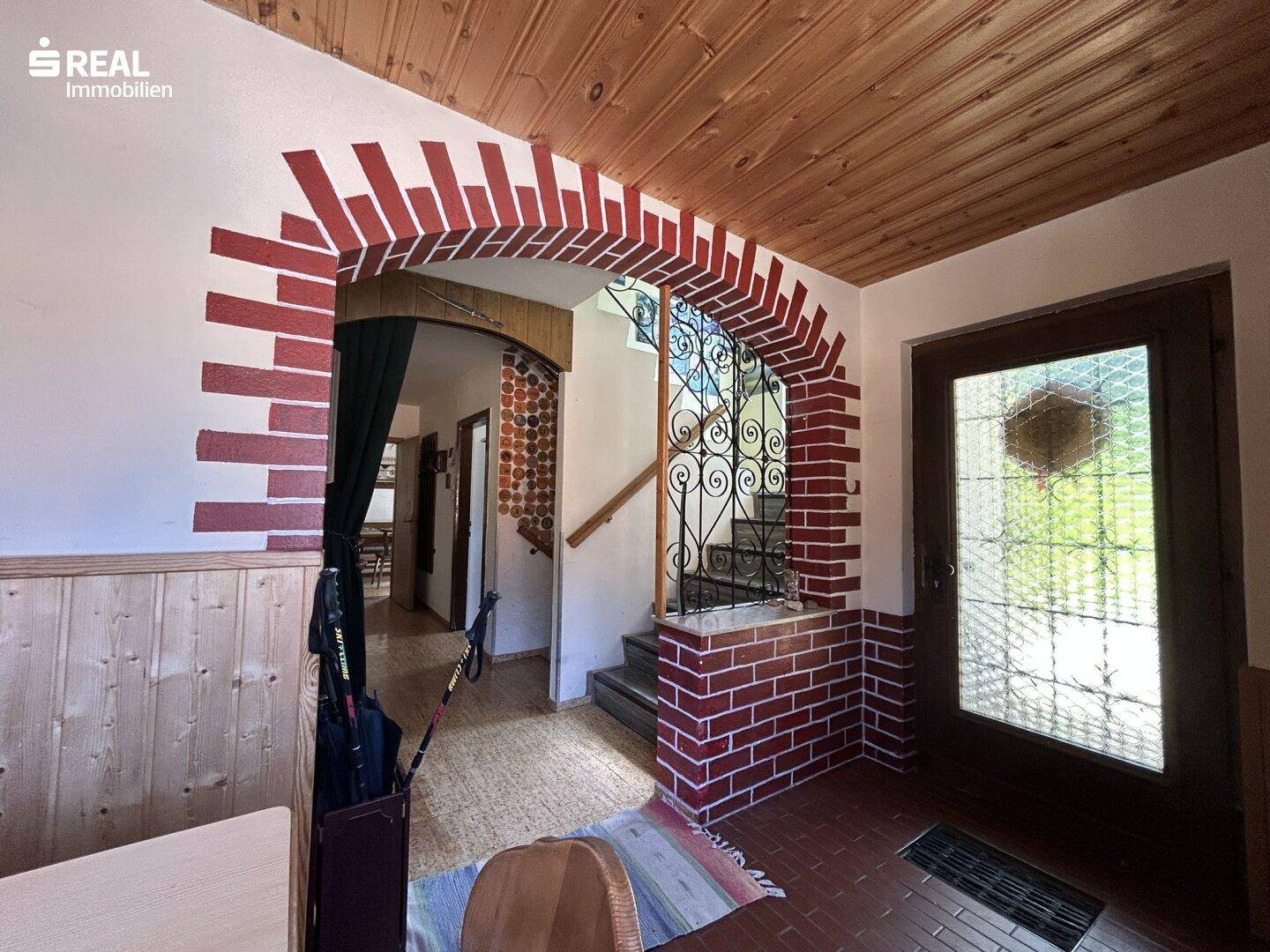 Rustikaler Eingangsbereich mit Ziegelbogen, Holzdecke und gefliestem Boden.