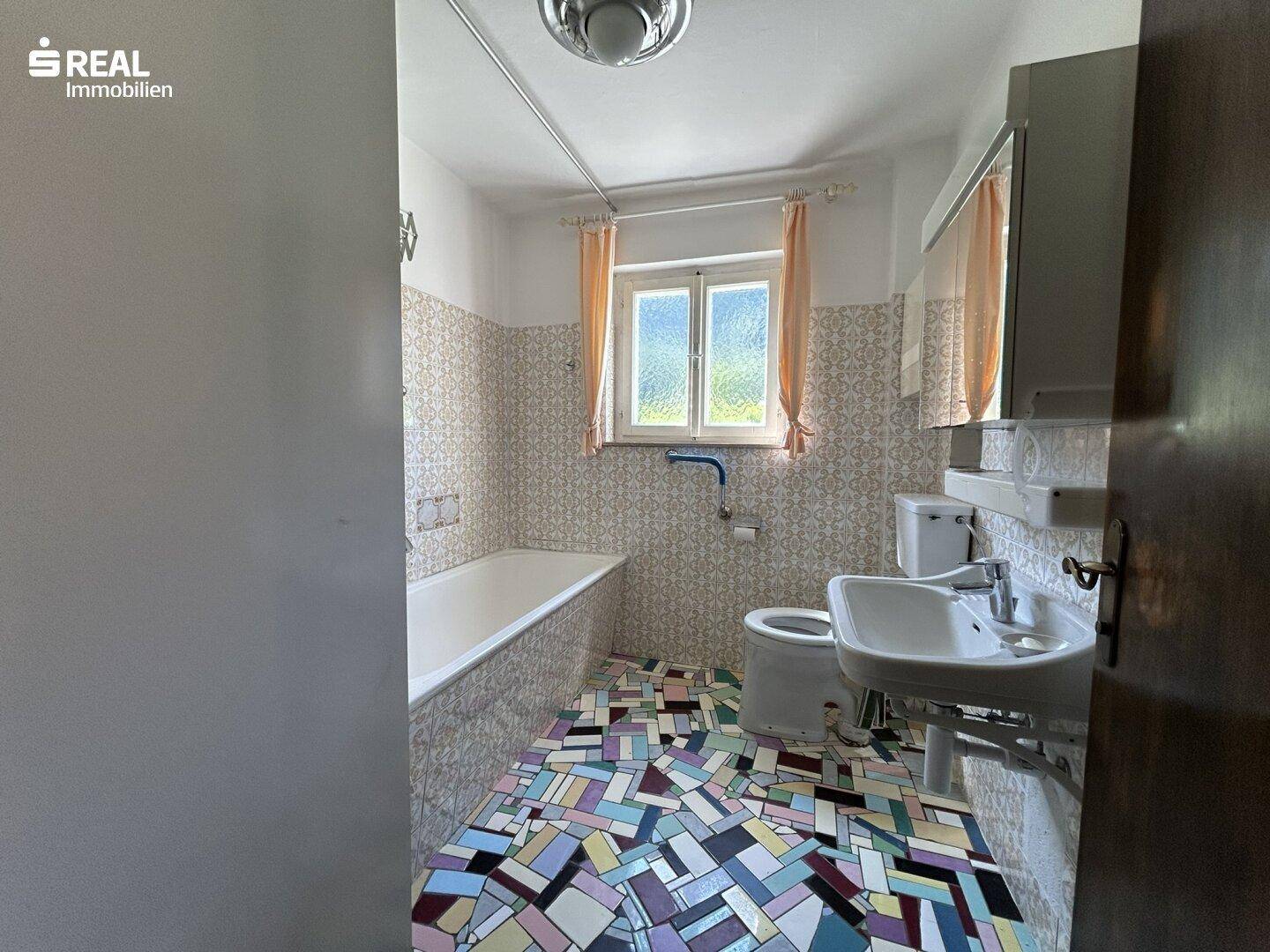 Badezimmer mit Badewanne, Waschbecken und farbenfrohen, gemusterten Fliesen an Wänden und Boden.