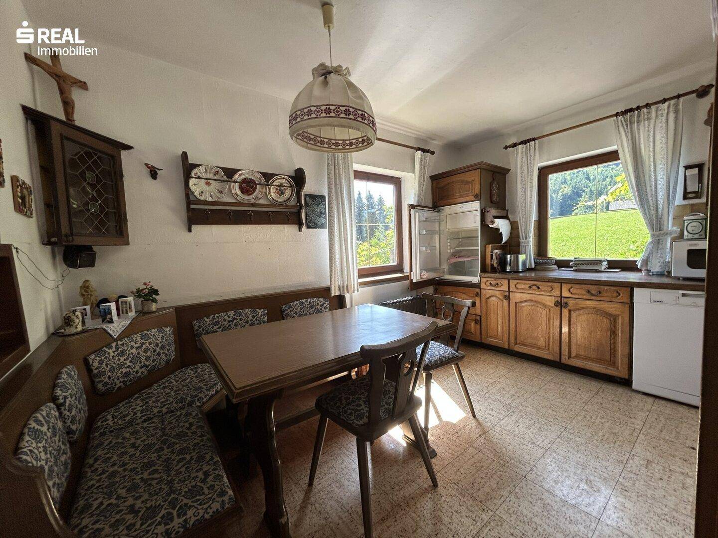 Traditionelle Wohnküche mit Holzschränken, Essbereich und Blick auf die grüne Landschaft.