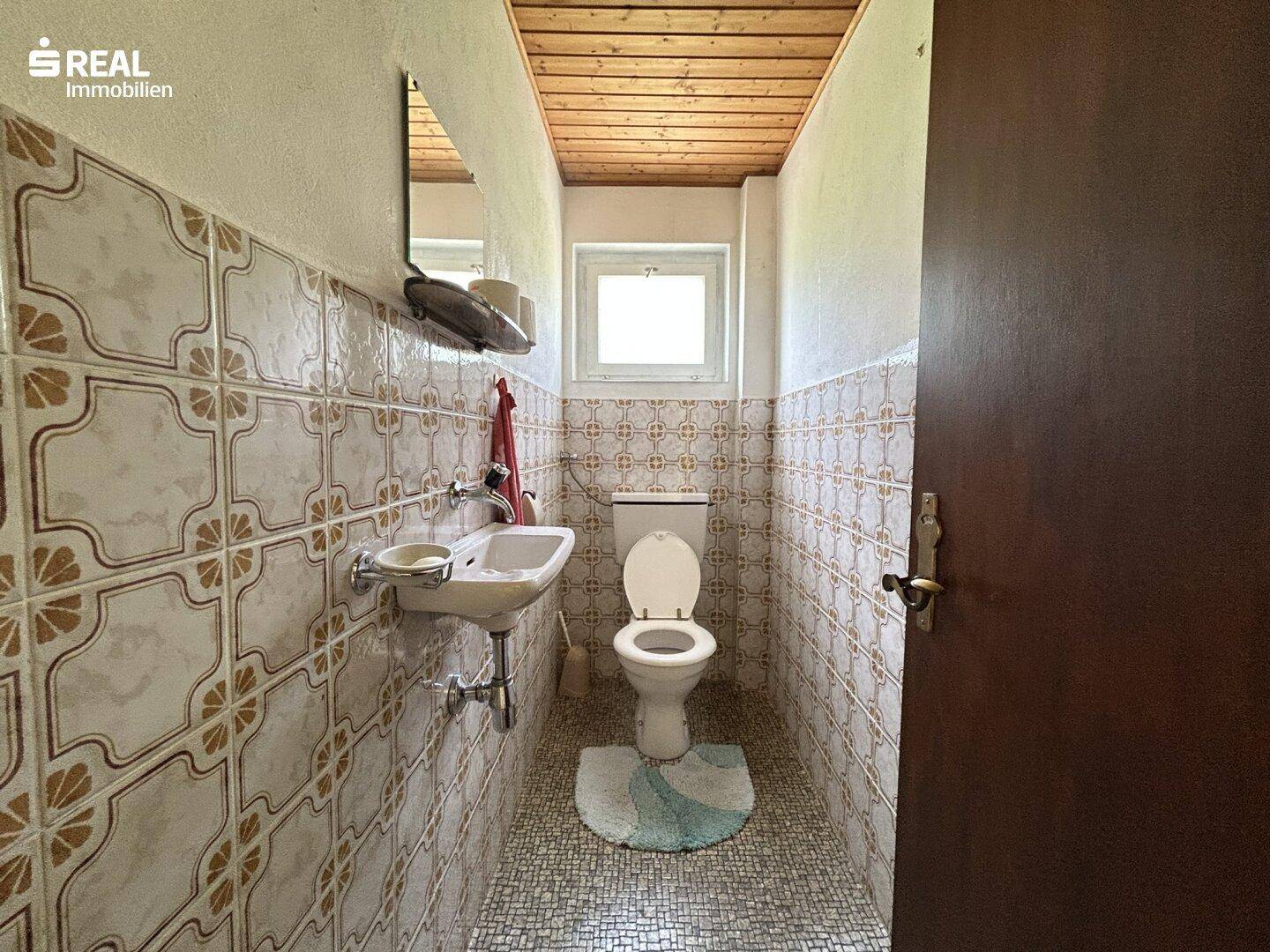 Separates WC mit Waschbecken und gemusterten Fliesen an Wänden und Boden.