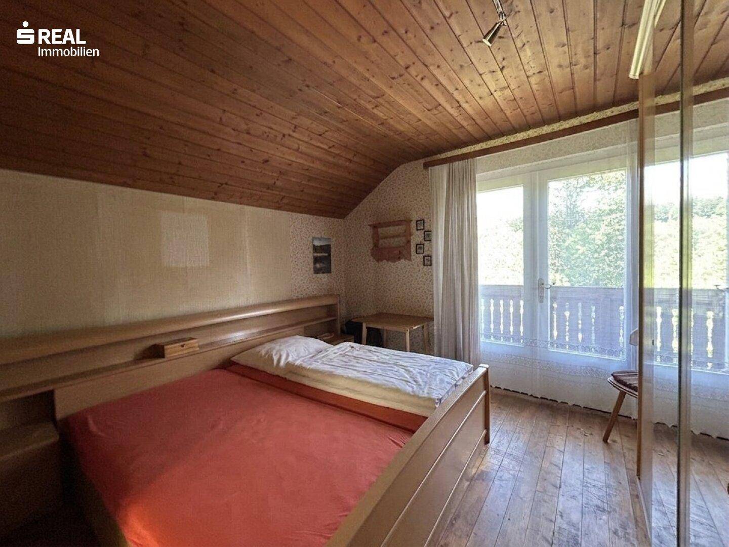 Schlafzimmer mit Holzboden und Holzdecke, ausgestattet mit einem Doppelbett und französischem Balkon.
