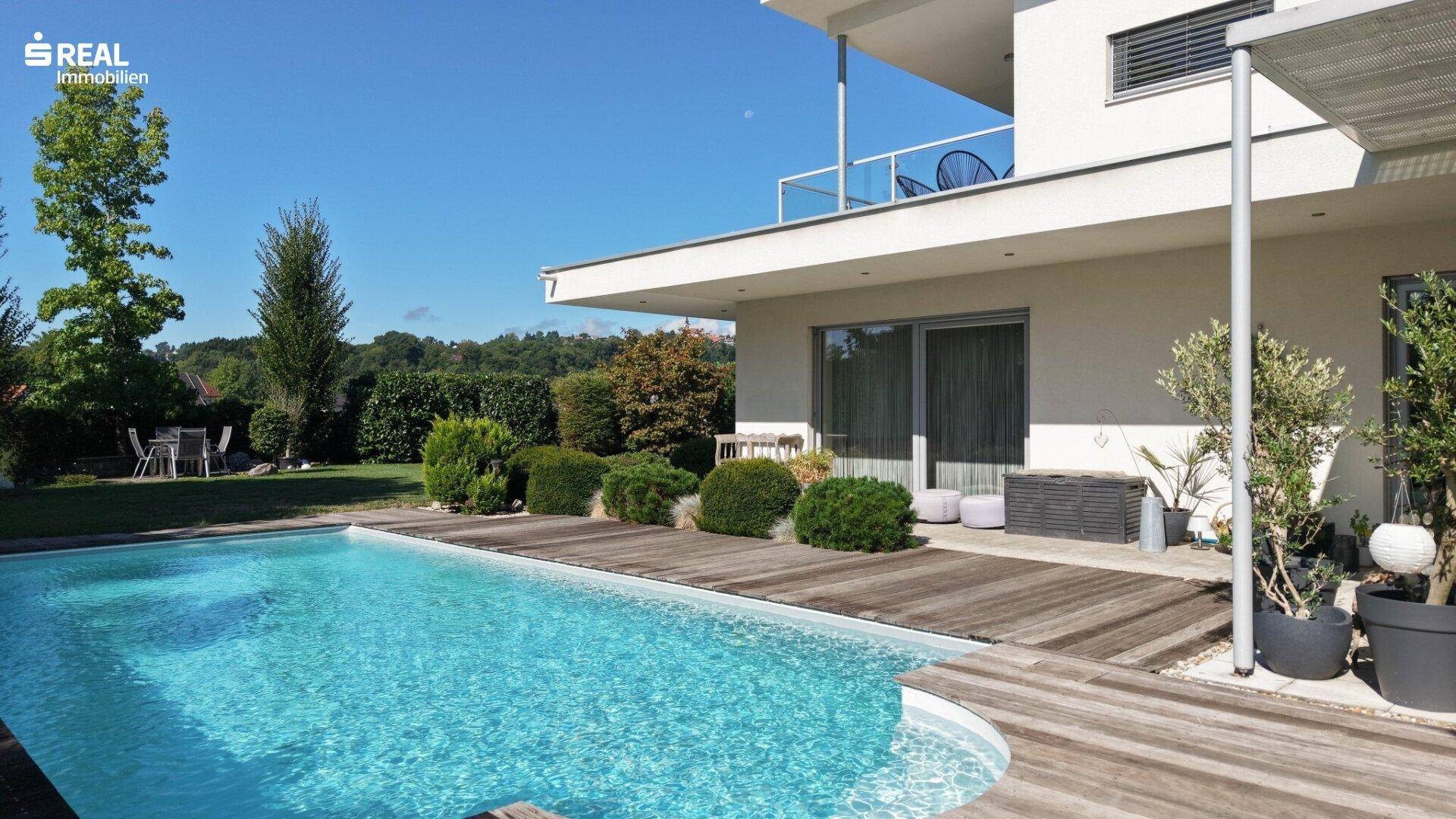 Seitlicher Blick auf den Poolbereich mit Holzdeck und der modernen Architektur des Hauses.