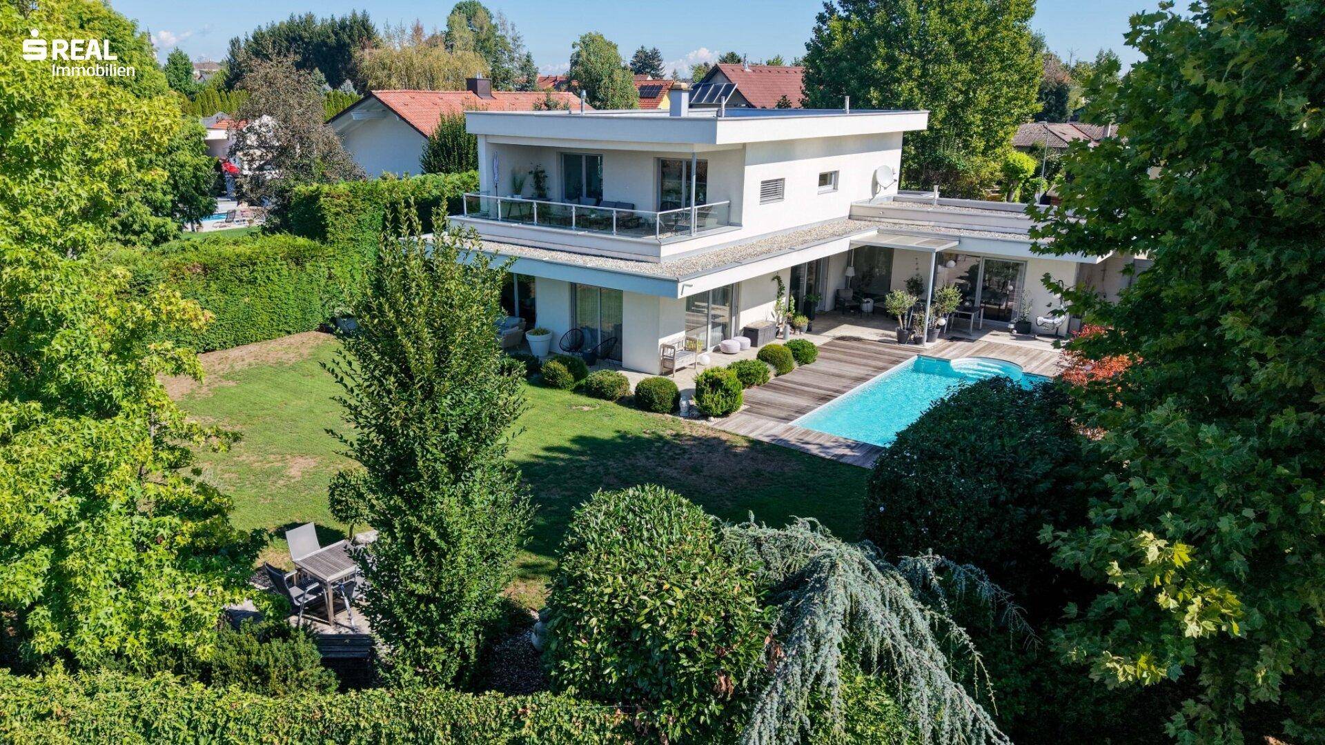 Vogelperspektive auf die moderne Villa mit großem Garten, Pool und umliegender grüner Landschaft.