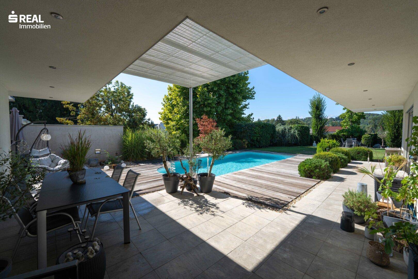 Überdachte Terrasse mit Essbereich und Blick auf den Pool und den grünen Garten.