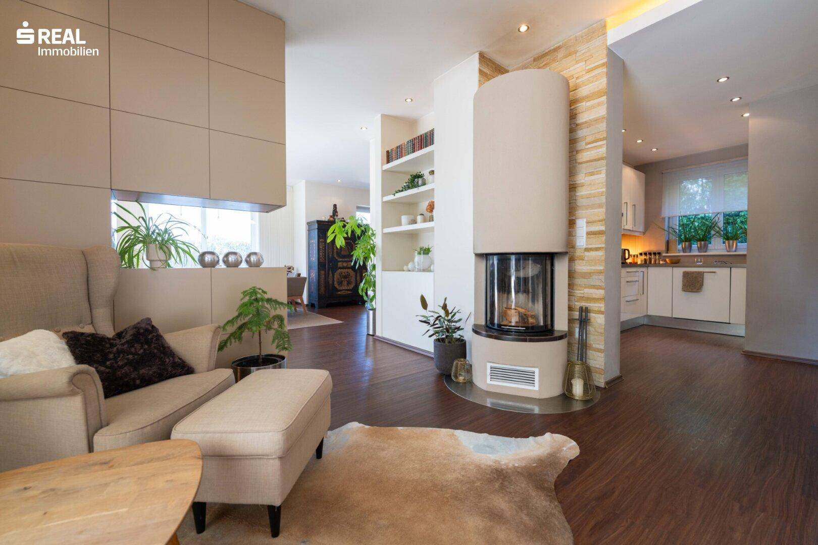 Heller Wohnbereich mit modernem Kamin, Holzboden und Blick in die Küche.