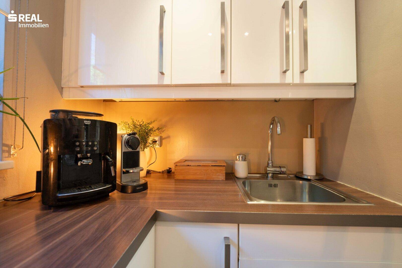Küchenzeile mit Holz-Arbeitsplatte, Spüle und moderner Kaffeemaschine.