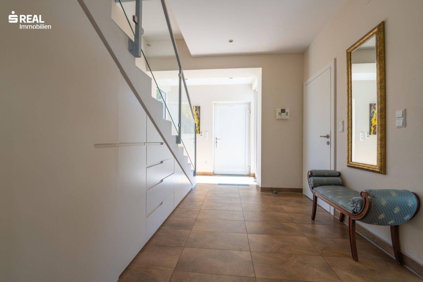 Heller Flur mit moderner Treppe, Einbauschränken und Fliesenboden.