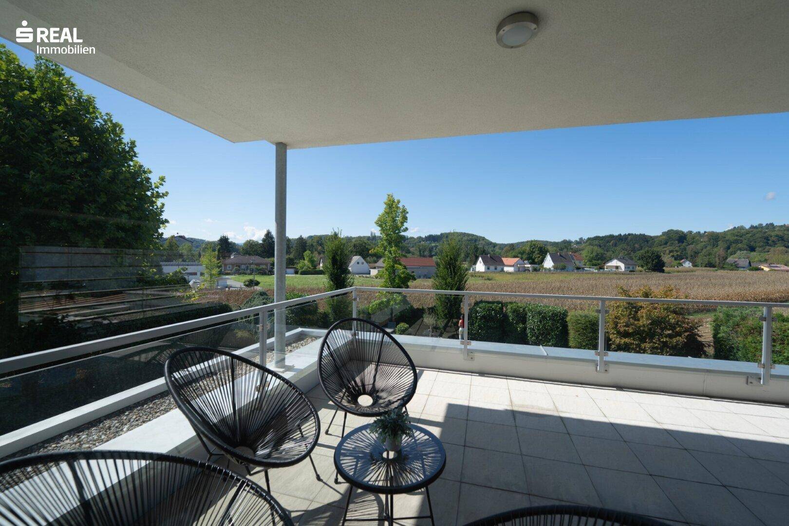 Heller Balkon mit modernen Sitzmöbeln und Panoramablick auf die grüne Umgebung.