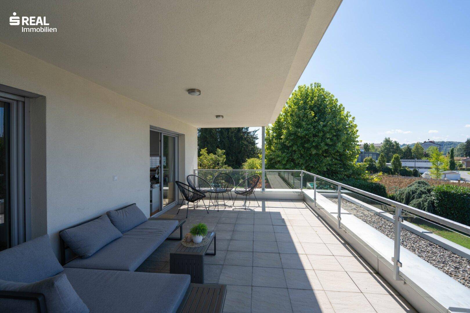 Geräumiger Balkon mit Lounge-Möbeln, Fliesenboden und weitem Blick ins Grüne.