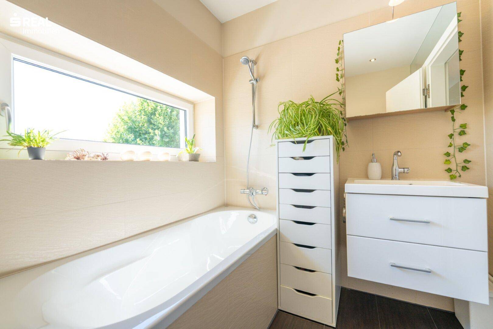 Helles Badezimmer mit Badewanne, Fenster und modernem Waschtischunterschrank.