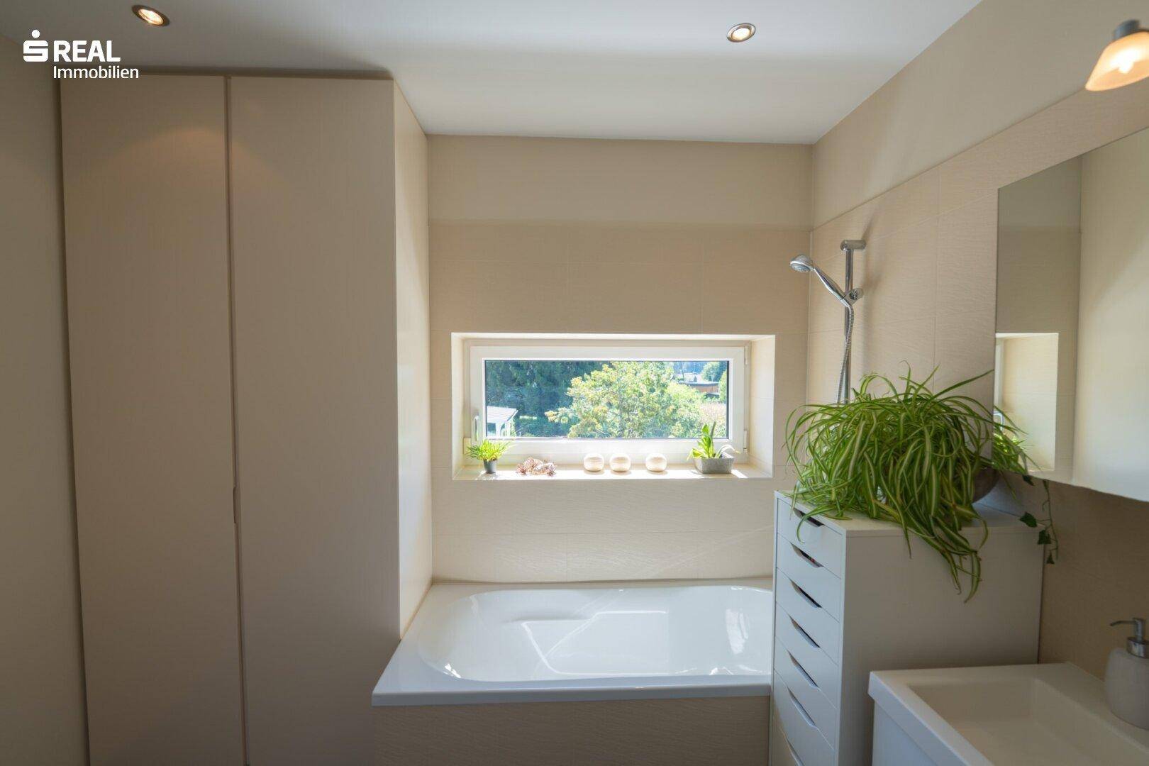 Modernes Badezimmer mit Badewanne, Fenster und integrierten Schränken.