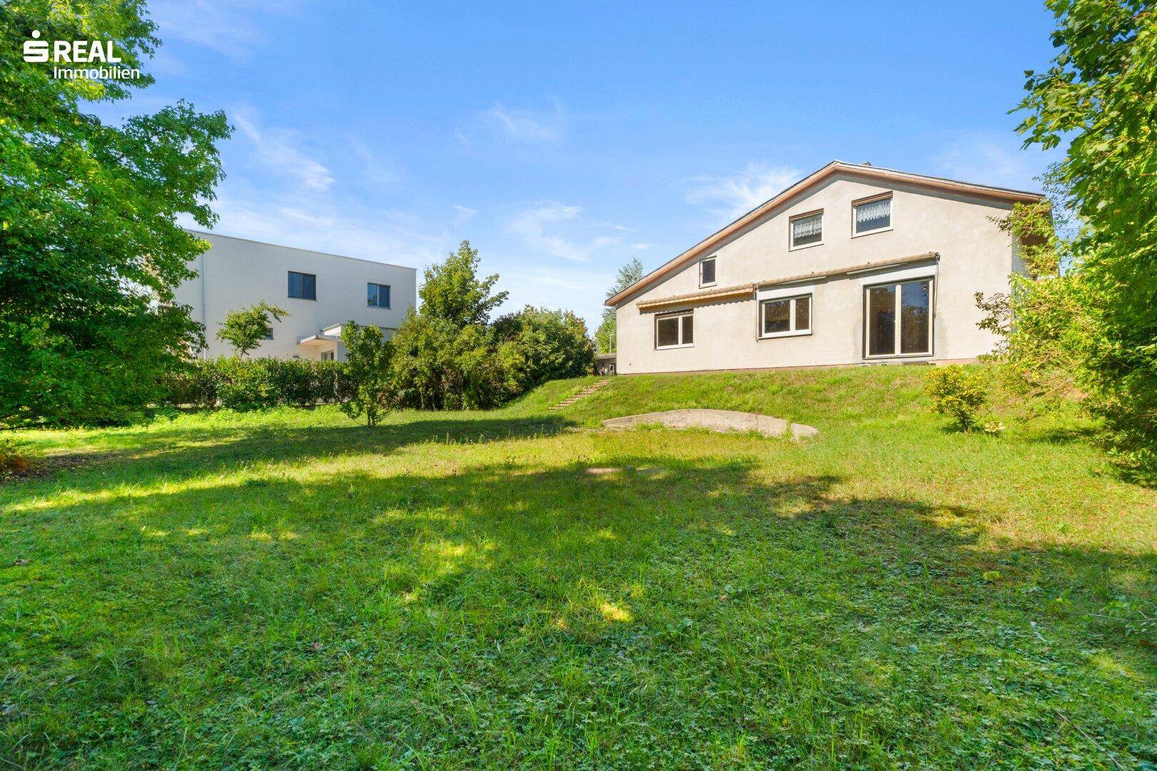 Rückansicht des Einfamilienhauses mit großem Garten und angrenzendem Neubau.