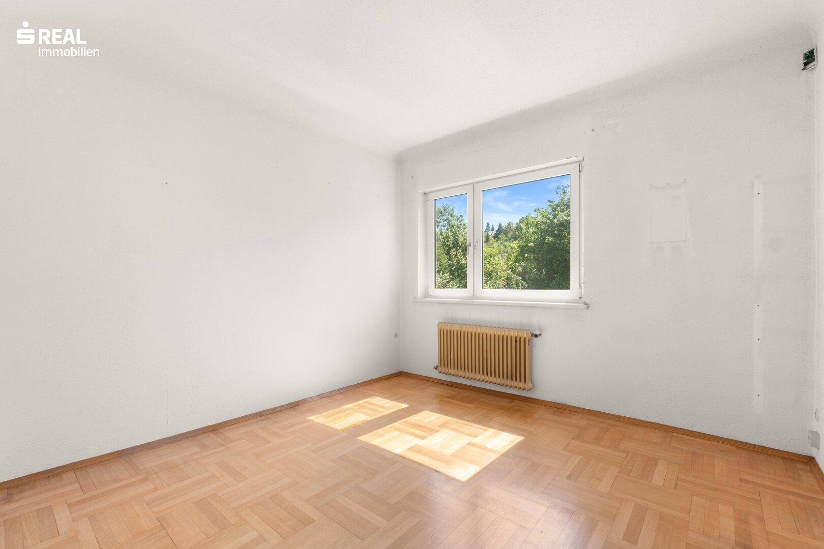 Lichtdurchflutetes Zimmer mit Parkettboden und Fenster, das viel Tageslicht hereinlässt.