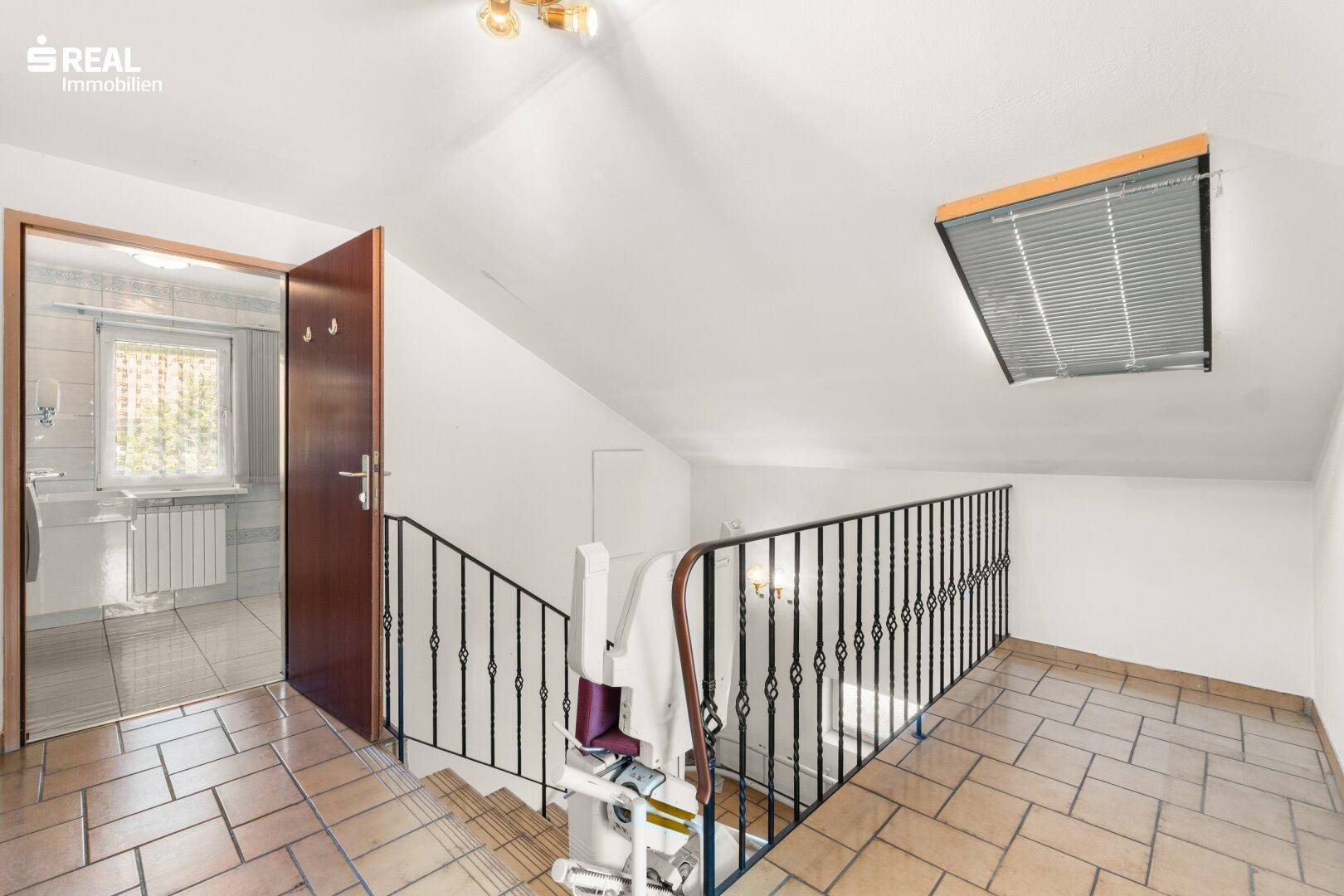 Treppenaufgang zum Obergeschoss mit Fliesenboden und Blick in ein angrenzendes Badezimmer.