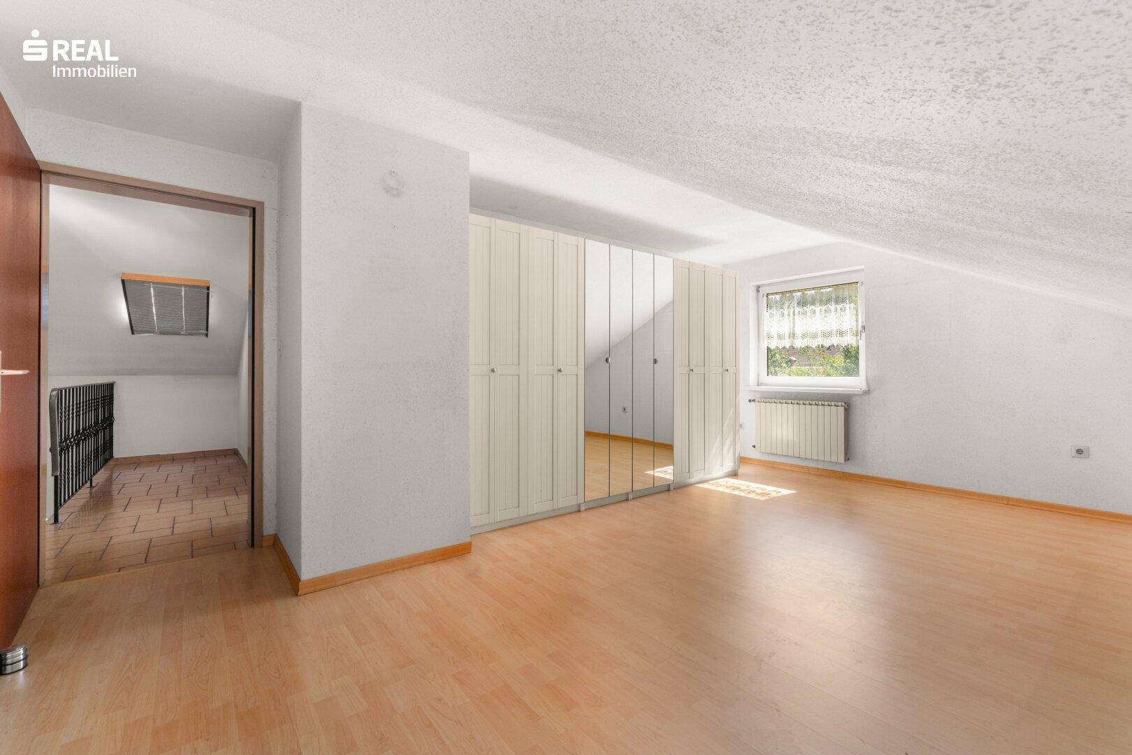 Dachgeschosszimmer mit Schrägen, Laminatboden und praktischen Einbauschränken.