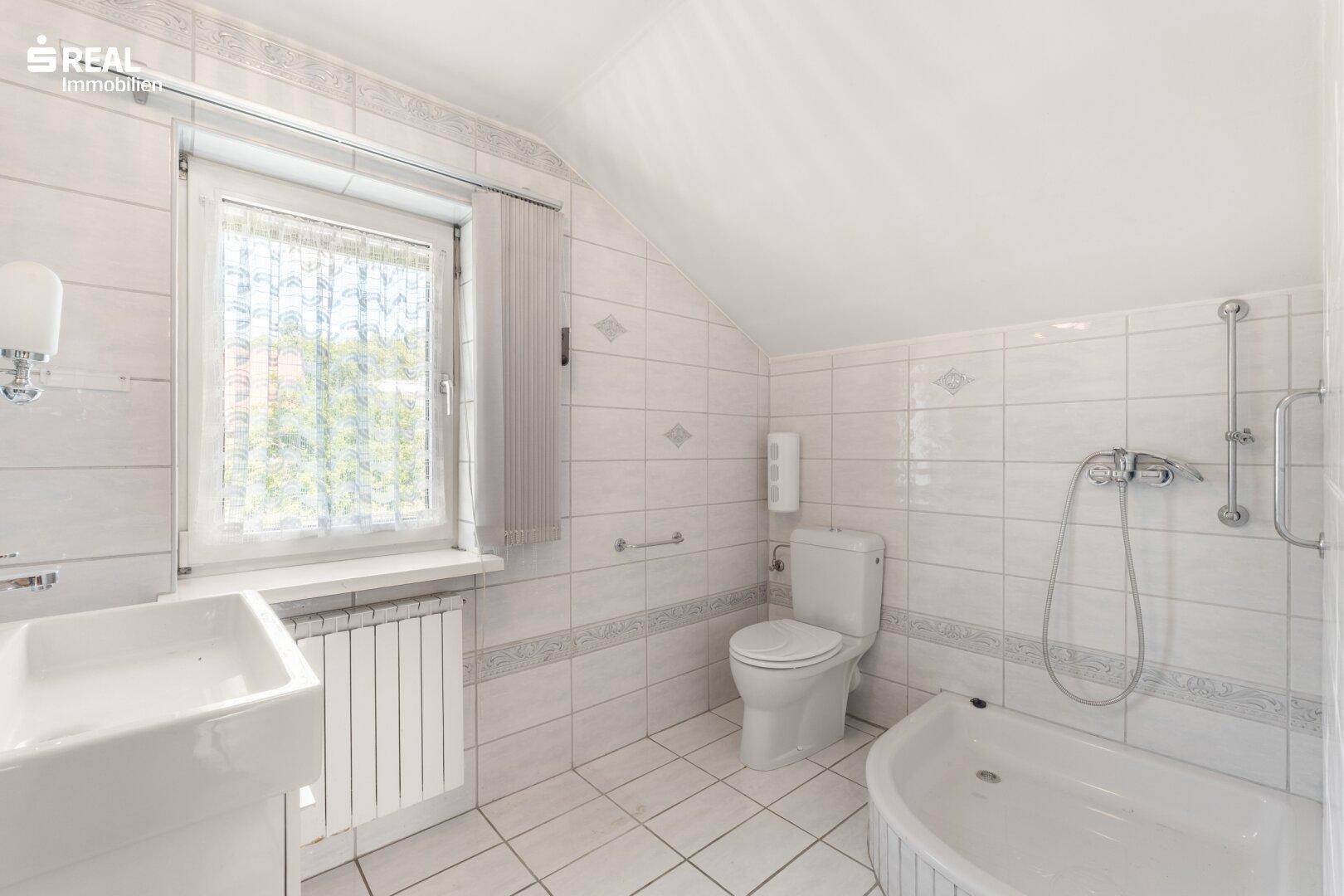 Dachgeschoss-Badezimmer mit Badewanne, WC, Waschbecken und Haltegriffen für Komfort.