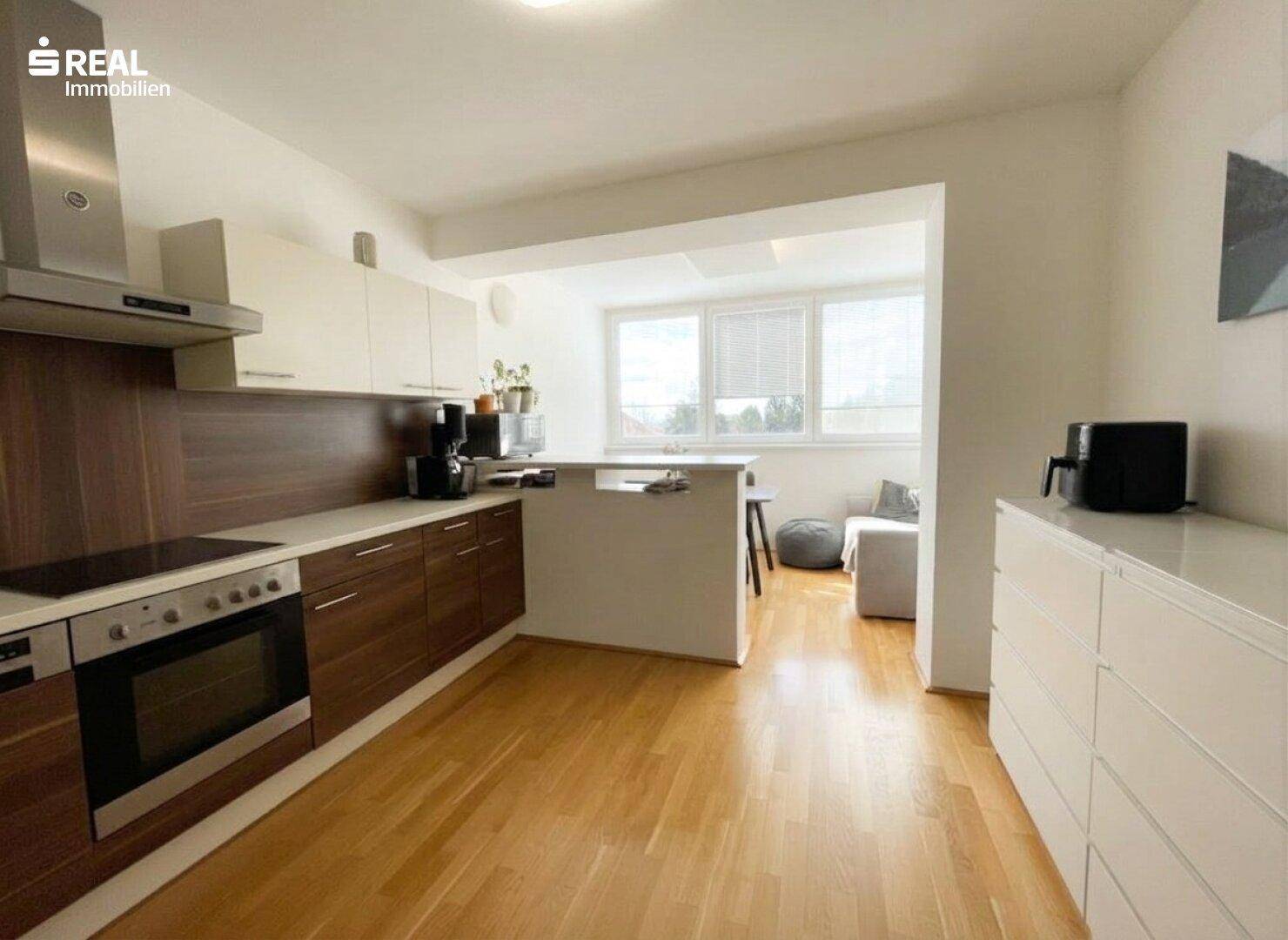Moderne Küche mit Holzboden und offener Verbindung zum hellen Wohnbereich.