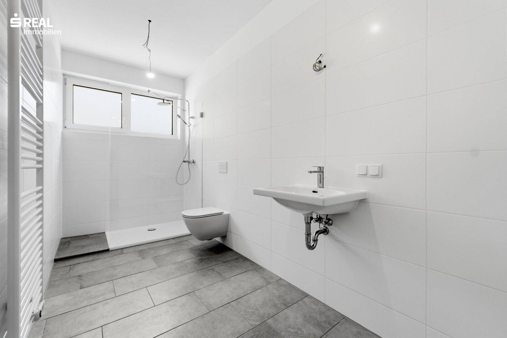 Modernes Badezimmer mit Dusche, Waschbecken, WC und beheiztem Handtuchhalter.