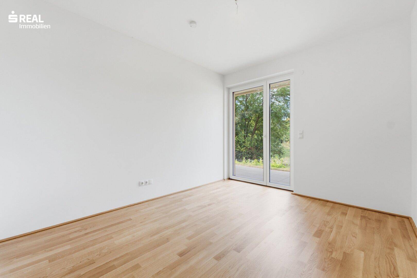 Heller, unmöblierter Raum mit Holzboden und Zugang zum Außenbereich.