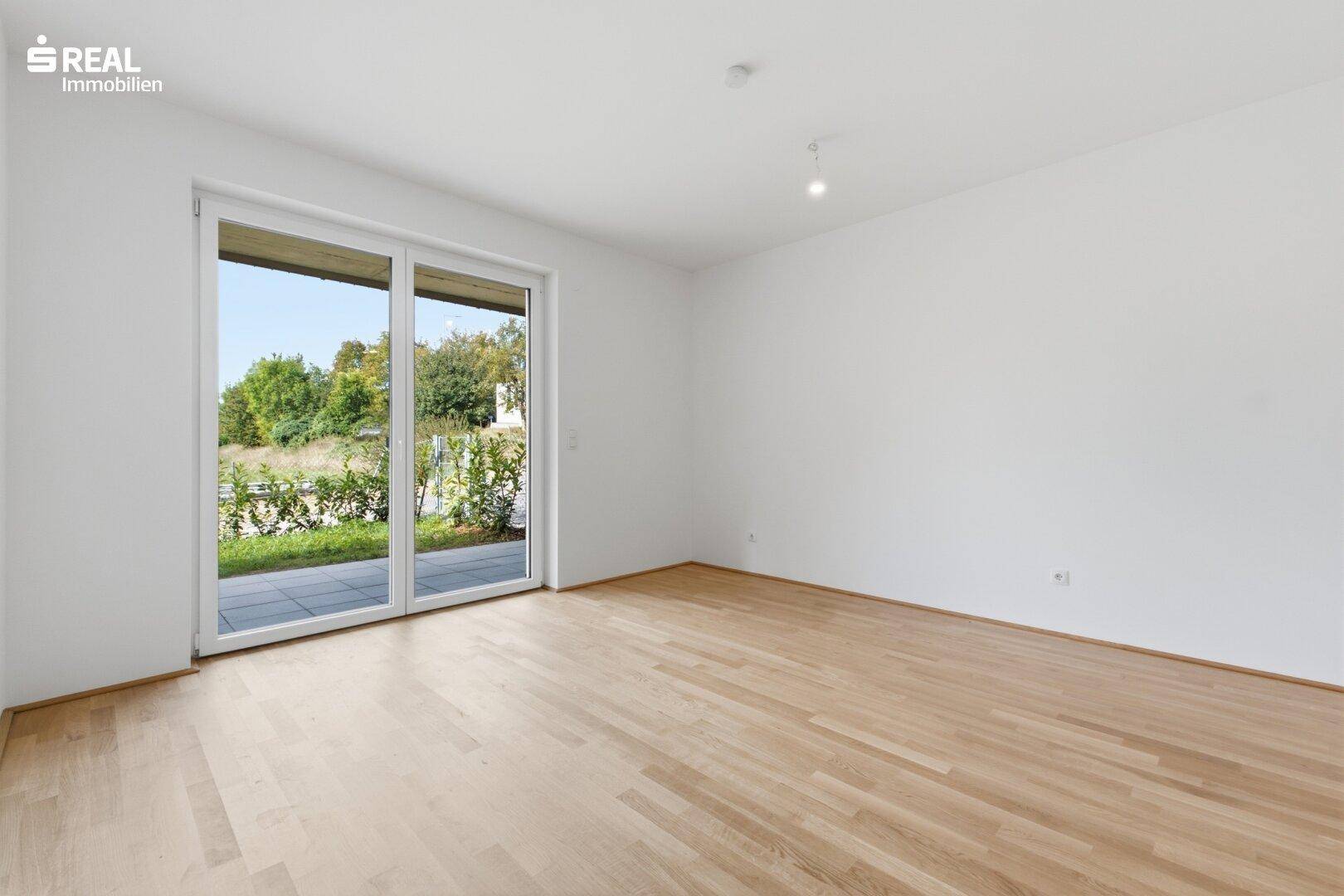 Geräumiger, heller Raum mit Holzboden und großer Fenstertür zum Garten.