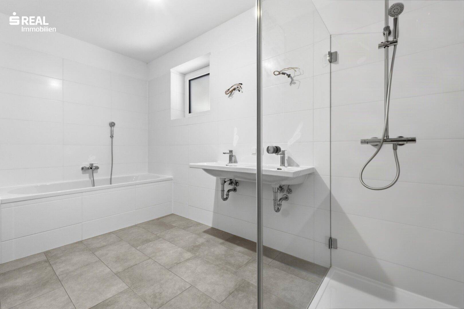 Helles Badezimmer mit Badewanne, Dusche, Doppelwaschbecken und Fenster.
