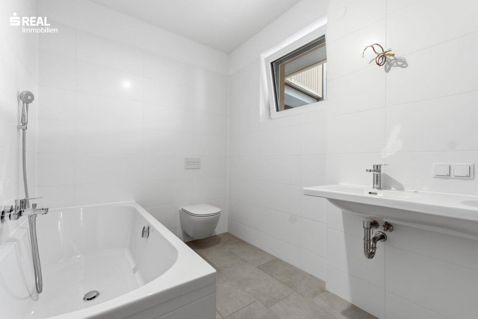 Modernes Badezimmer in Weiß mit Badewanne, wandhängendem WC, Waschbecken und einem kleinen Fenster.