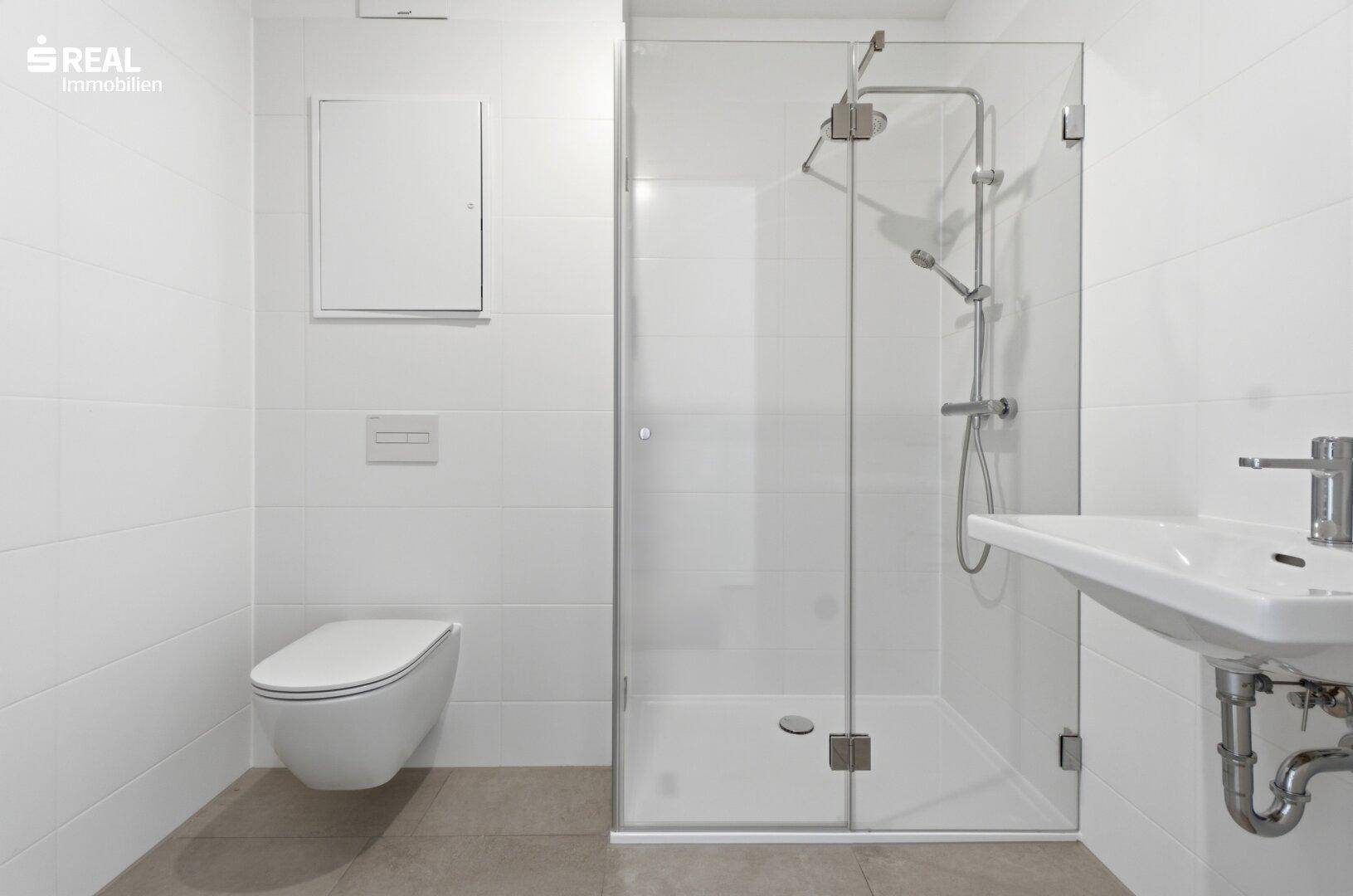 Helles Badezimmer mit moderner Duschkabine, wandhängendem WC und Waschbecken, alles in Weiß gehalten.
