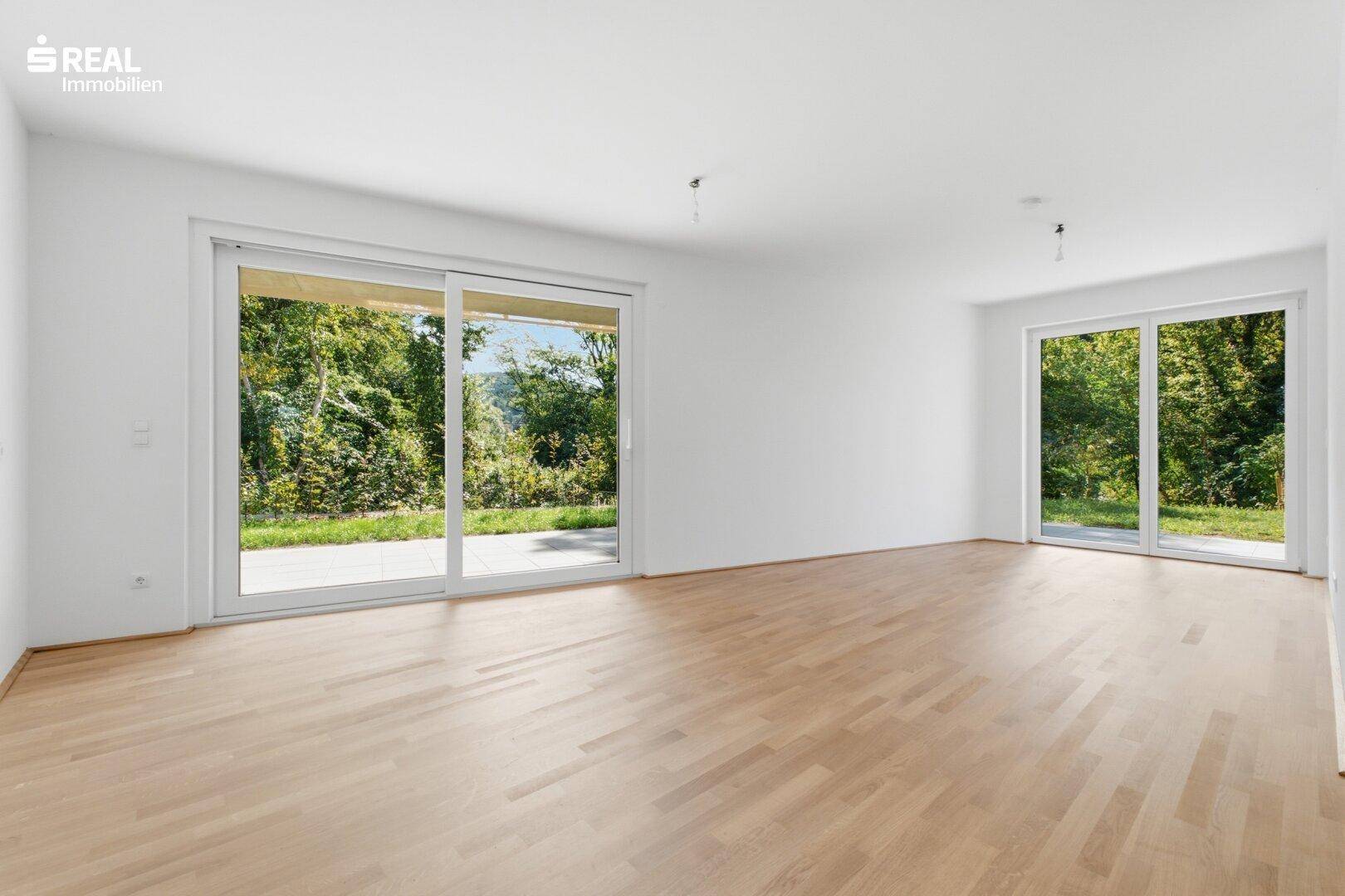 Heller, leerer Wohnraum mit Holzboden und großen Schiebetüren, die Zugang zum Garten bieten.