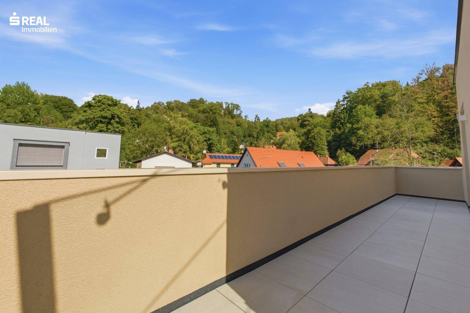 Kleine Terrasse mit Fliesenboden und Blick über die Dächer und Baumwipfel.