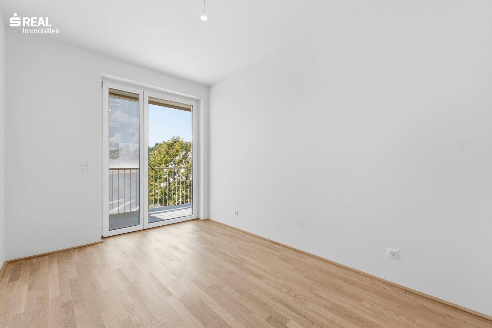 Leeres Schlafzimmer mit Holzparkett und Balkonzugang, hell und freundlich.