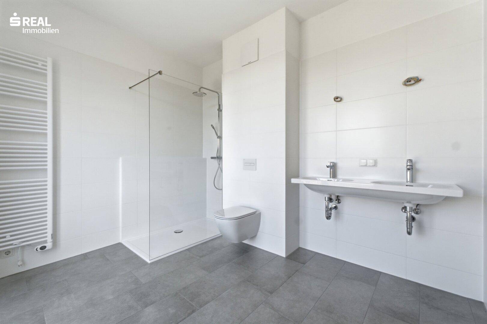 Modernes Badezimmer mit Doppelwaschbecken, großer Dusche und Handtuchheizkörper.
