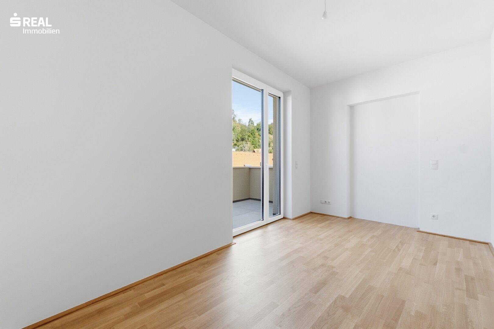 Helles Zimmer mit Parkettboden und Zugang zu einem kleinen Balkon.