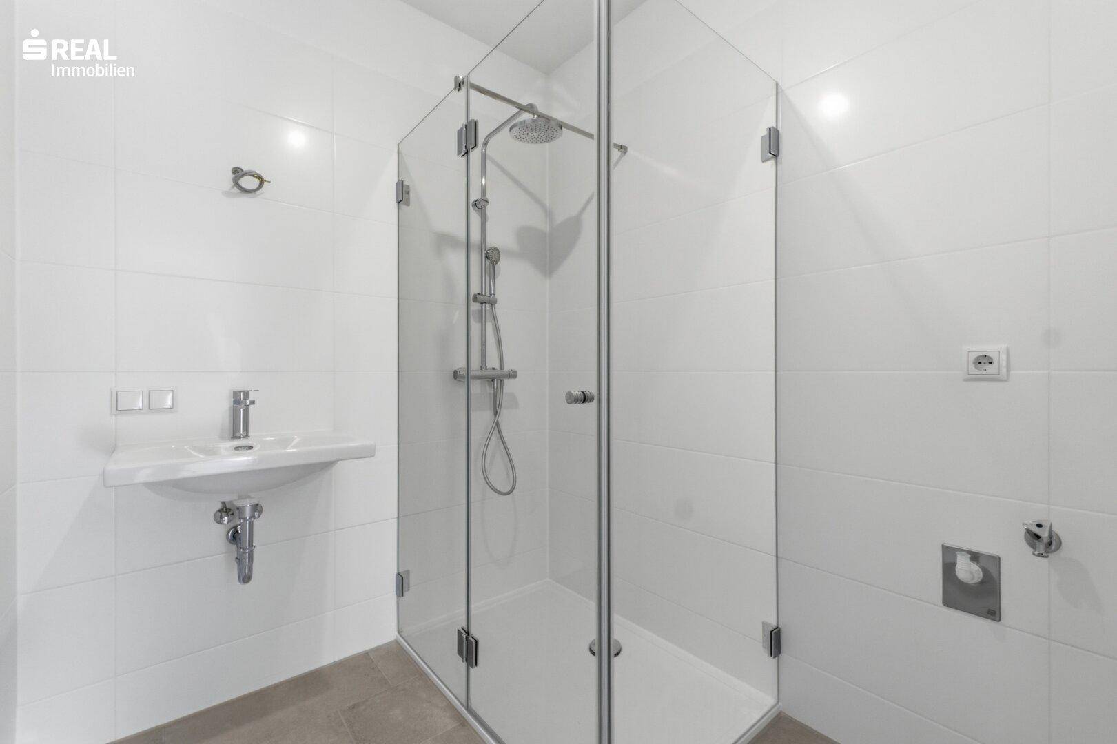 Helles Badezimmer mit weiß gefliesten Wänden, moderner Duschkabine und Einzelwaschbecken.