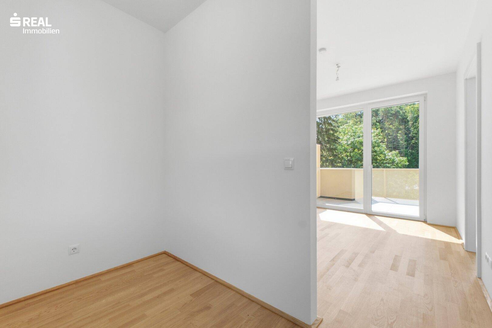 Heller, leerer Raum mit Parkettboden und Blick auf den Außenbereich.